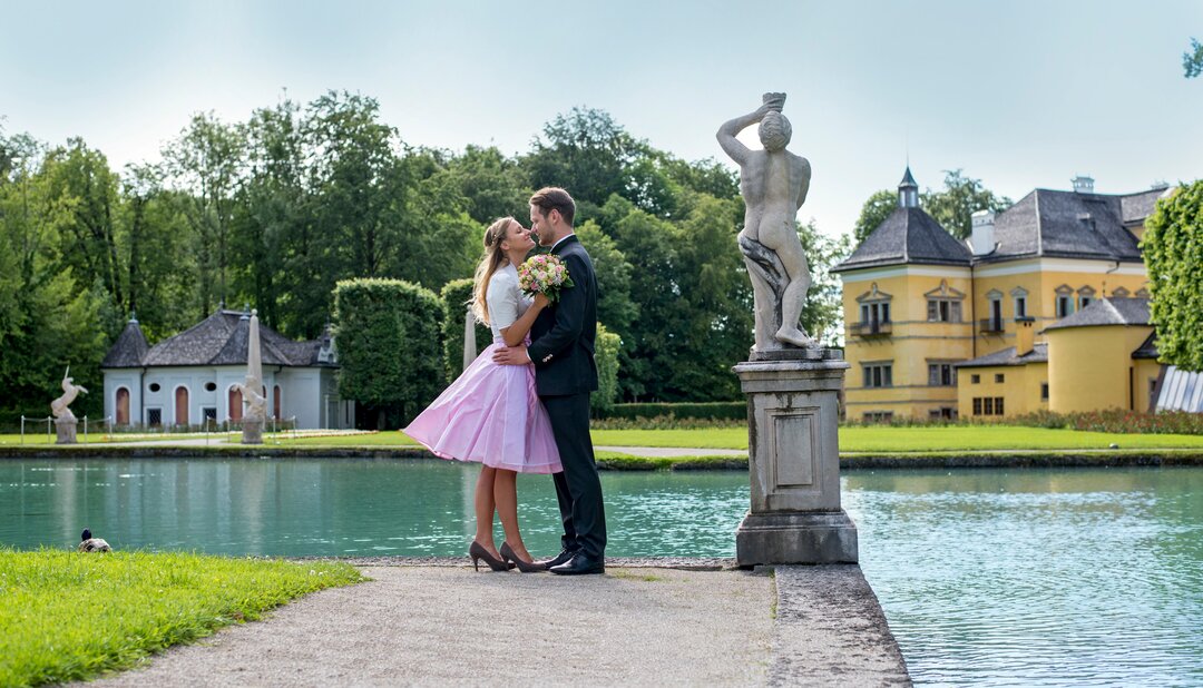 Happy wedding couple on the water level in Hellbrunn Palace Park | © scheinast.com